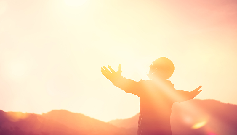 Man stretching arms and looking at the sun “looking positively towards the future” (photo)